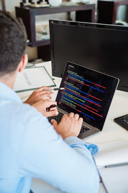 Photograph showing a close-up view of a computer screen displaying colorful lines of programming code, including JavaScript syntax, with a focus on the script elements. The screen is part of an indoor