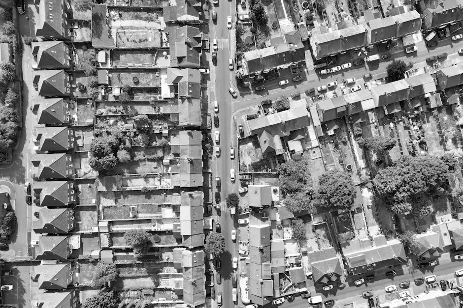 An aerial view of a residential neighbourhood showing rows of terraced houses and detached homes with small front and back gardens. Cars are parked along the narrow streets and driveways, with some ve